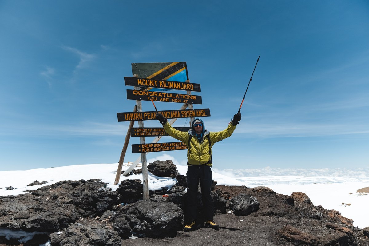 A trekker celebrating at the Uhuru Peak summit sign on Mount Kilimanjaro, Tanzania
